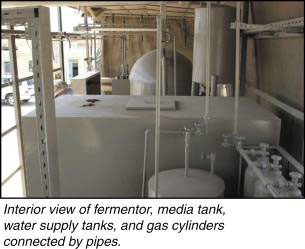 Interior view of a fermentor, media tank, water supply tanks, and gas cylinders connected to pipes.